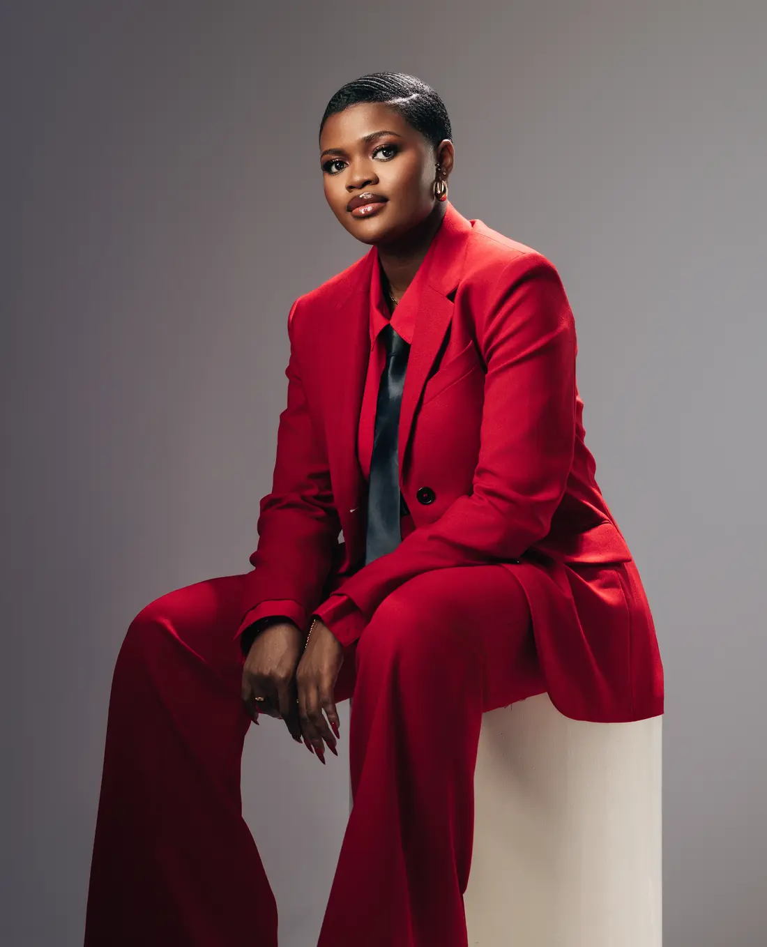 Kweyakie seated in a red suit and black tie