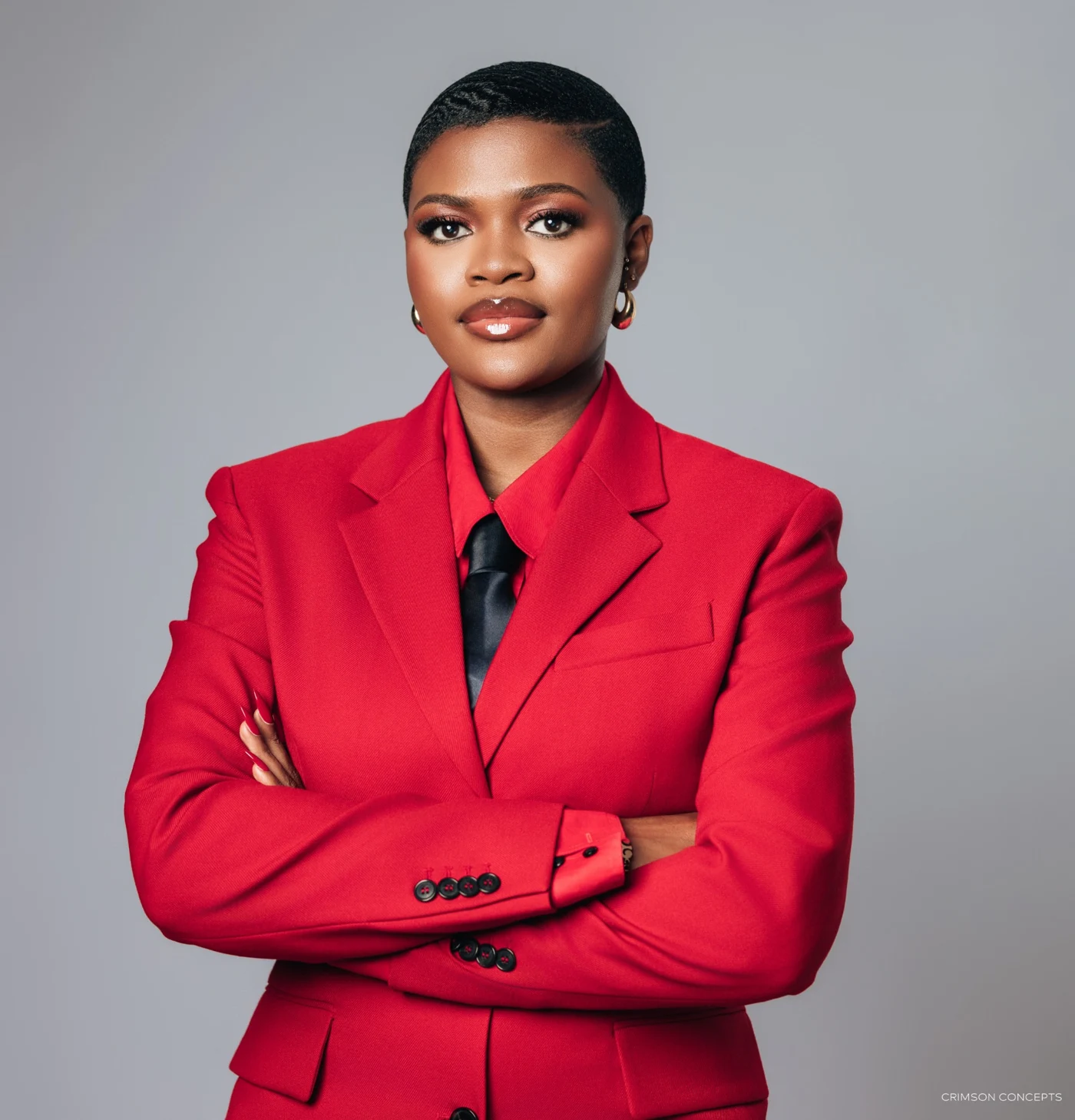 Kweyakie in a red suit, arms folded, full portrait